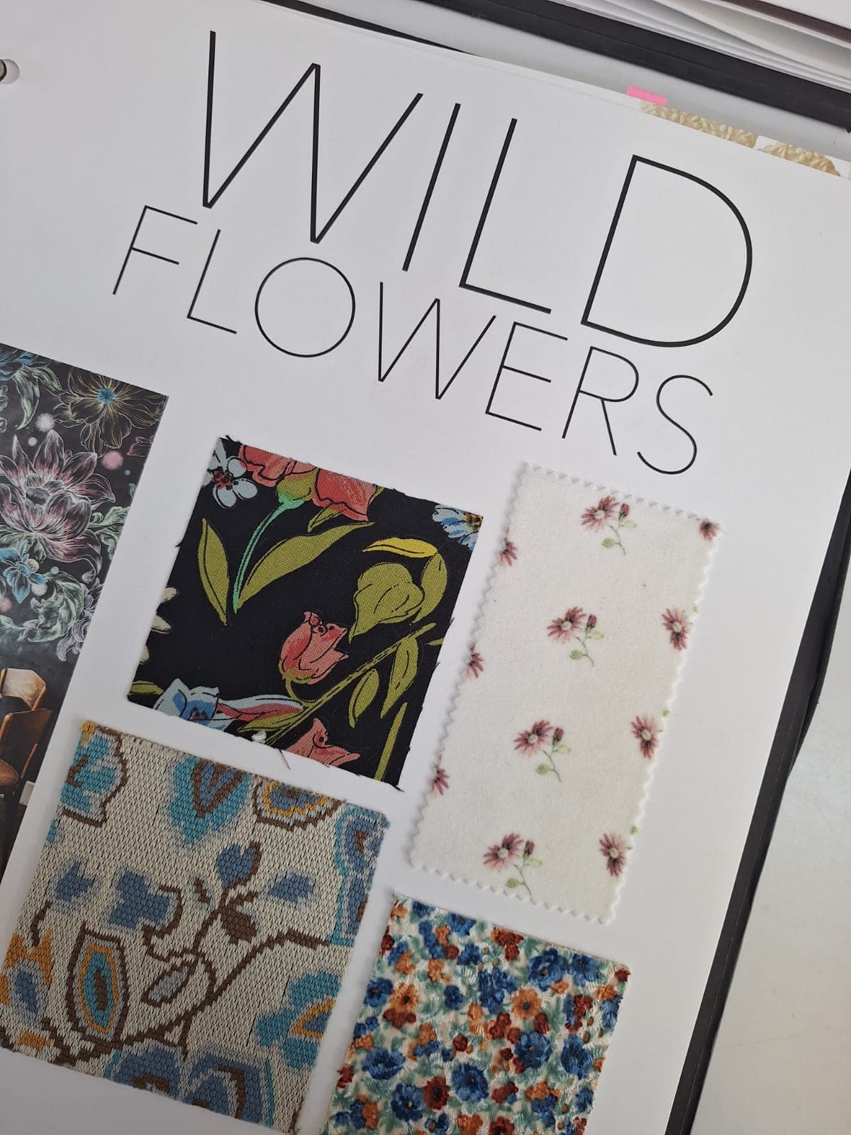 An open swatch book titled "WILD FLOWERS" featuring several fabric samples, including a dark floral pattern, a light fabric with pink daisies, a blue and orange paisley fabric, and a multicolored fabric with small flowers.